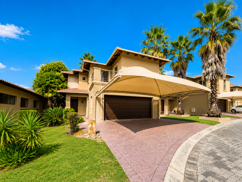 Front elevation of a residential property featuring a paved driveway, a large shade sail carport, and a double garage.