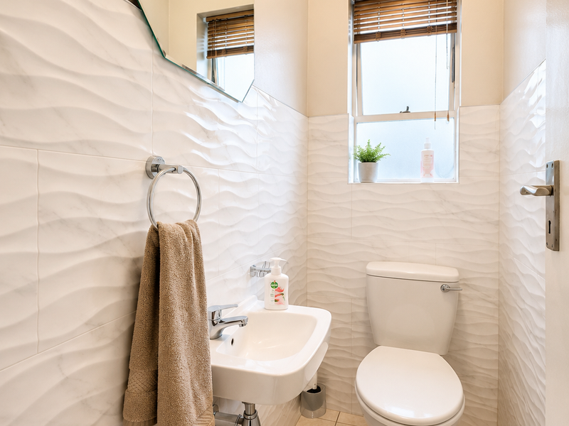 A compact, modern guest bathroom featuring white textured wall tiles, a wall-mounted basin, and a standard toilet.