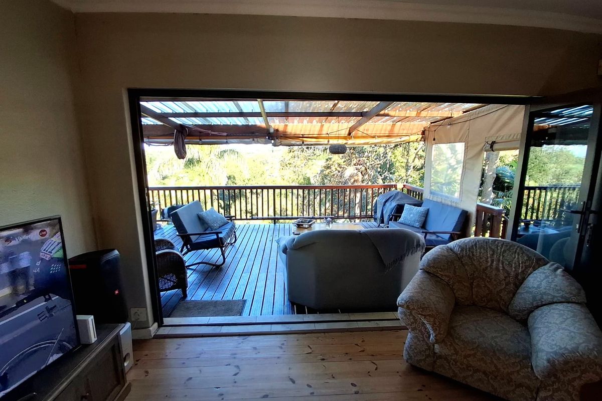Living room featuring timber flooring and large sliding doors opening onto an elevated timber deck with a covered outdoor entertainment area.
