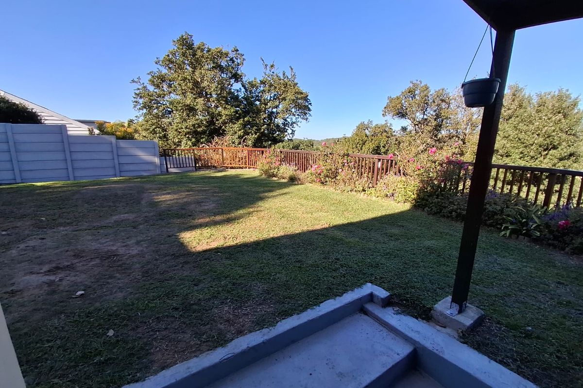 A rear garden area featuring a concrete patio, timber balustrade, and a precast concrete boundary wall overlooking a lawn.