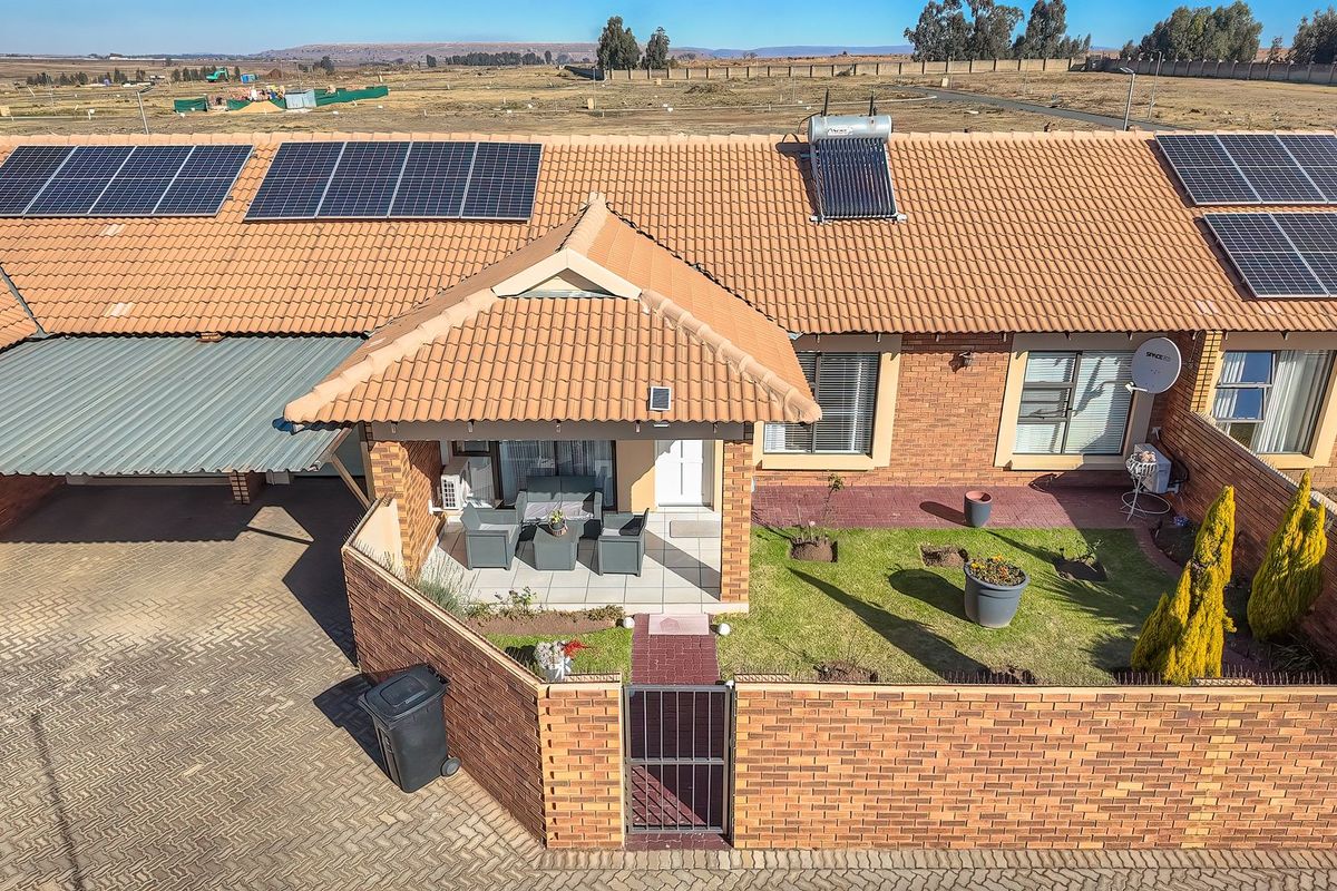 Aerial view of a cluster home featuring a tiled roof with solar panels, a solar geyser, a private garden, and a covered patio entrance.