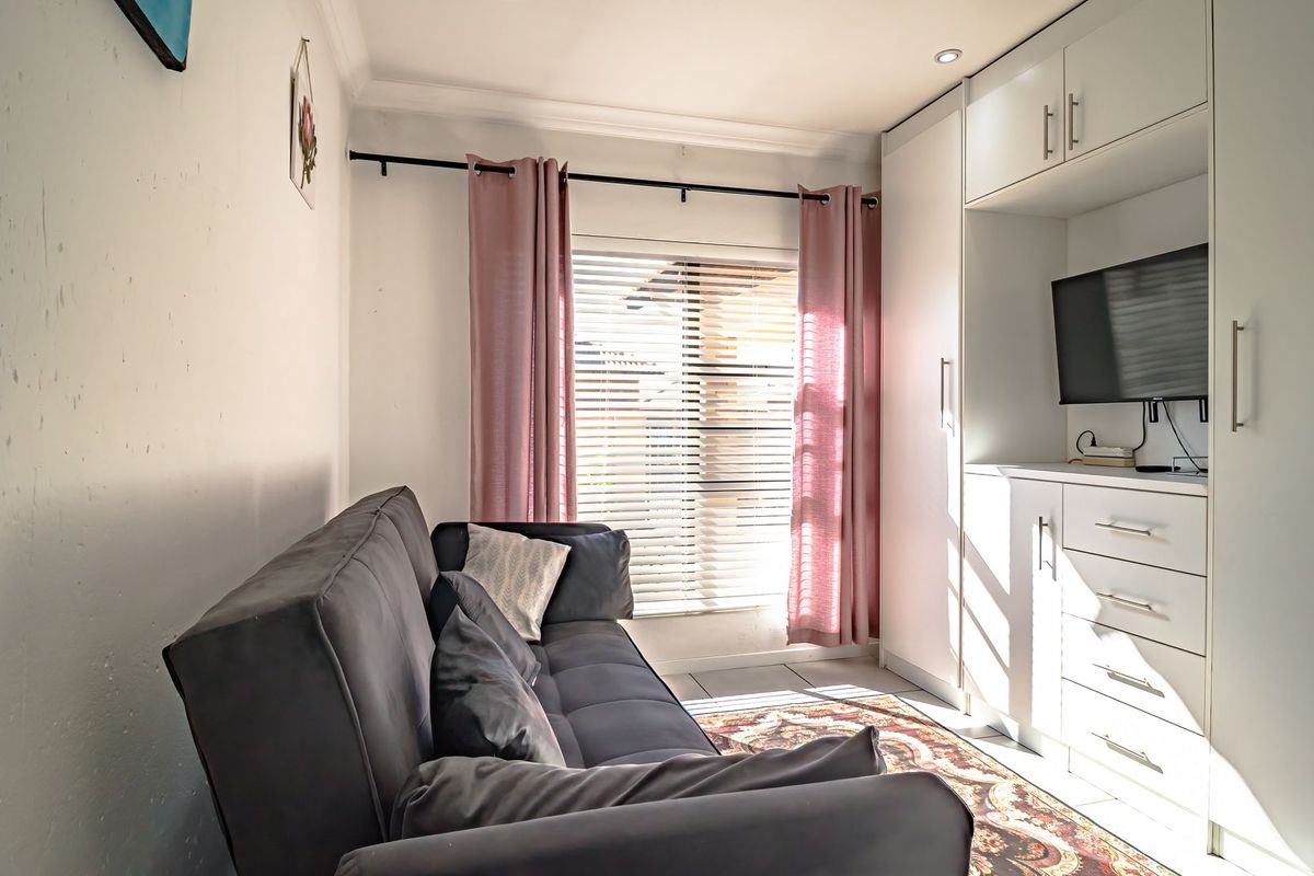 A compact bedroom featuring built-in white cabinetry, tiled flooring, and venetian blinds, offering functional storage and natural light.