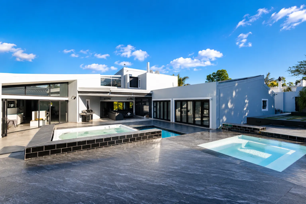 Modern rear exterior featuring a large tiled patio, swimming pool, and integrated spa, complemented by expansive bi-fold doors connecting to the interior living spaces.