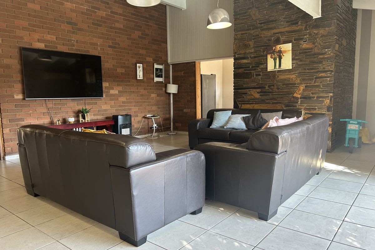 Spacious living room featuring a striking stone fireplace wall, exposed brickwork, vaulted ceilings, and neutral tiled flooring, offering a warm and textured aesthetic.