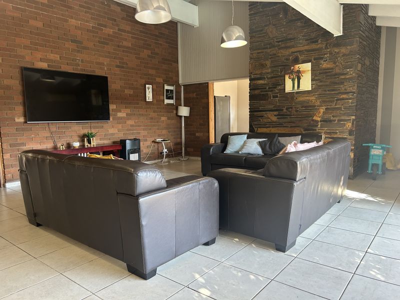 Spacious living room featuring a striking stone fireplace wall, exposed brickwork, vaulted ceilings, and neutral tiled flooring, offering a warm and textured aesthetic.