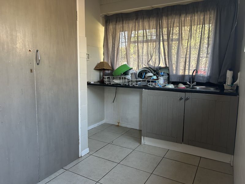 A functional laundry area featuring tiled flooring, built-in cabinetry, and a stainless steel sink with a tiled splashback.