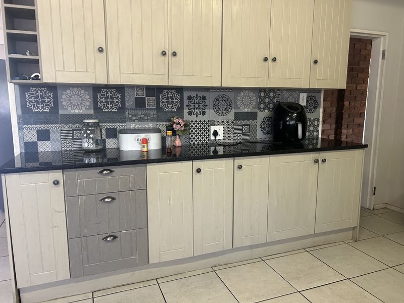 Kitchen featuring cream-toned cabinetry, black granite countertops, and a decorative patterned tile backsplash with ceramic floor tiles.
