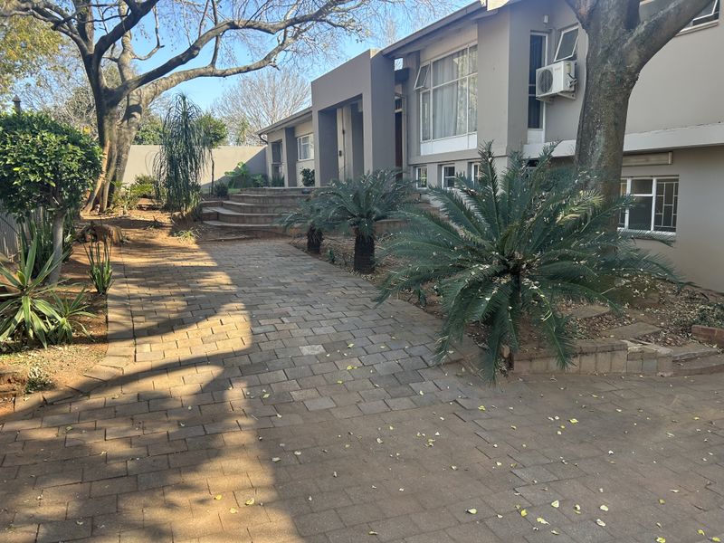 Front elevation of the property featuring a paved driveway, split-level entrance, and established garden landscaping with mature trees.