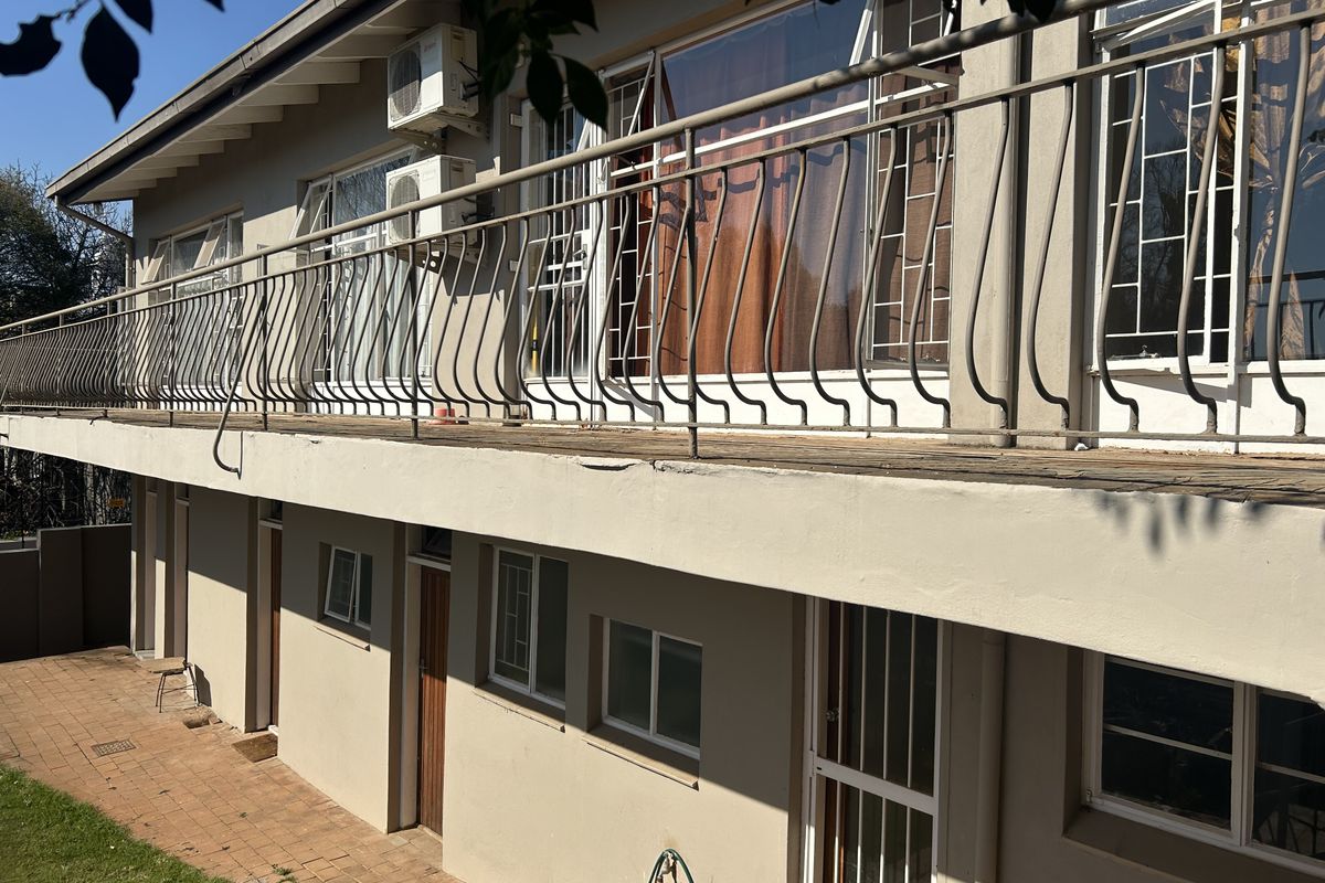Rear exterior view of the house featuring a long balcony with metal railings, paved patio area, and multiple access points to the interior.