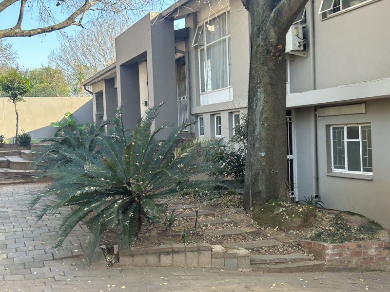 Front elevation of a multi-level residence featuring paved driveway, retaining walls, and established garden elements with security features.