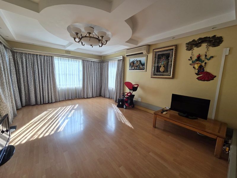Spacious living room featuring laminate flooring, a decorative recessed ceiling with integrated lighting, and a wall-mounted split-system air conditioner.