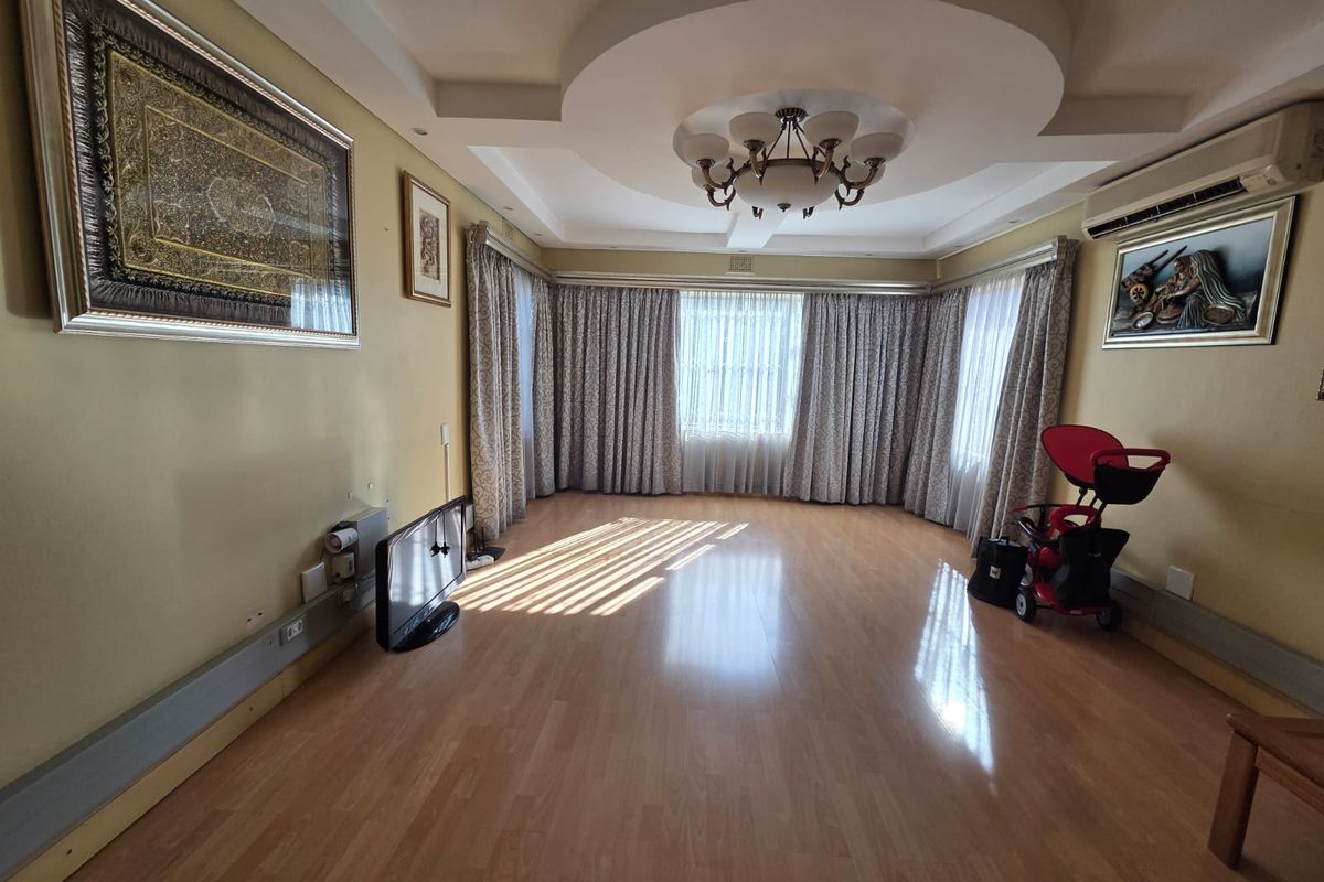 Spacious living room featuring laminate flooring, a decorative recessed ceiling with integrated lighting, and a wall-mounted air conditioning unit.