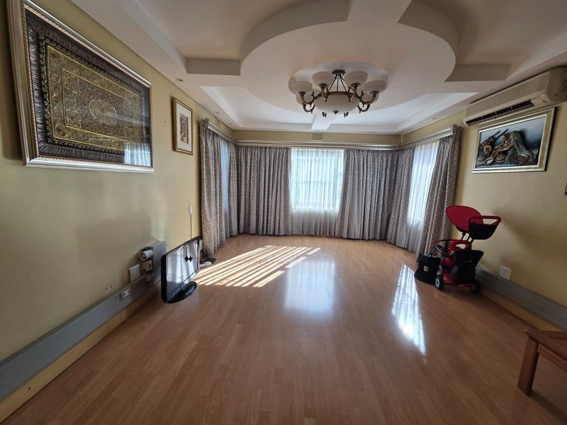 Spacious living room featuring laminate flooring, a decorative recessed ceiling with integrated lighting, and a wall-mounted air conditioning unit.