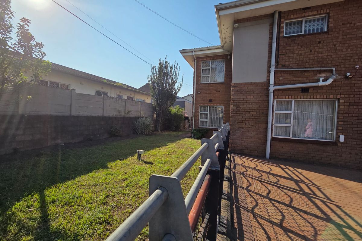 Rear view of the property featuring a brick facade, paved patio area, and a private garden enclosed by a boundary wall and security fencing.