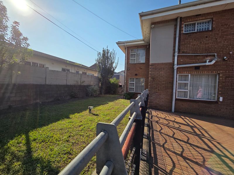 Rear view of the property featuring a brick facade, paved patio area, and a private garden enclosed by a boundary wall and security fencing.