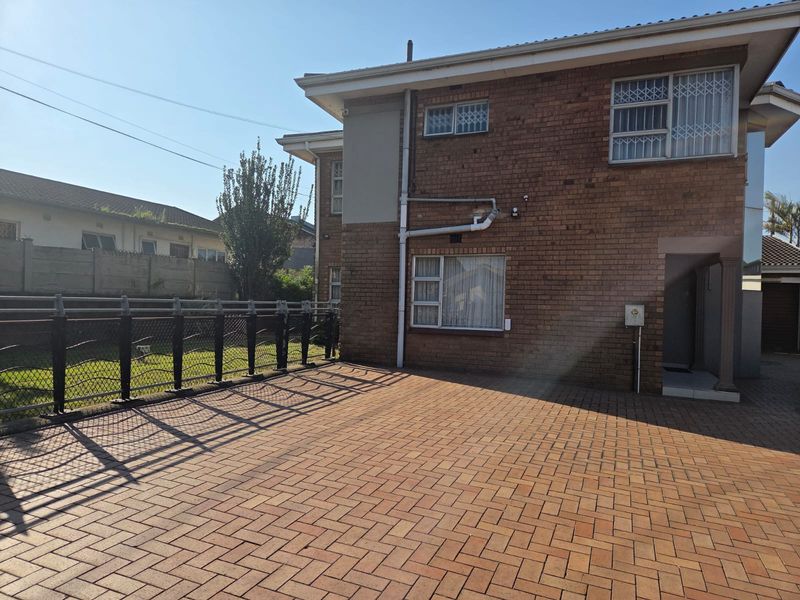 Rear view of the property featuring a brick facade, paved courtyard area, and perimeter fencing.