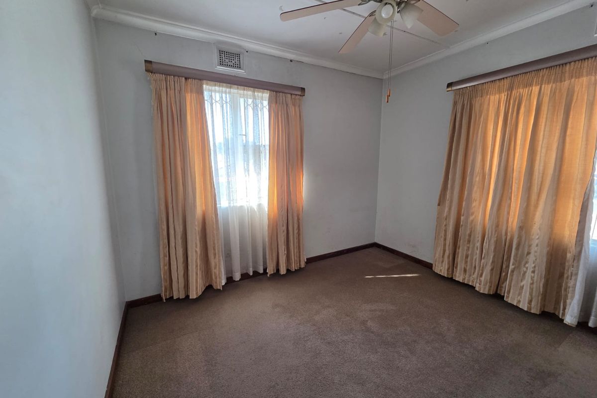 An empty bedroom featuring carpeted flooring, a ceiling fan, and classic cornice detailing, ready for renovation or restyling.