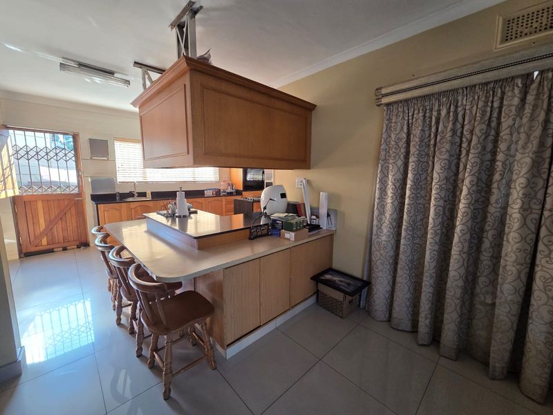 A functional kitchen featuring a central island with an overhead extractor fan, wooden cabinetry, granite countertops, and tiled flooring.