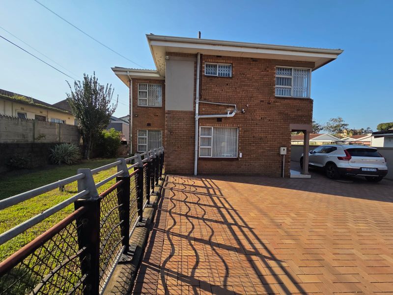 Two-story brick residential property featuring a paved driveway, security window bars, and a fenced garden area.