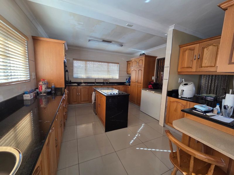 Spacious kitchen featuring wooden cabinetry, granite countertops, a central island with a built-in hob, and tiled flooring.