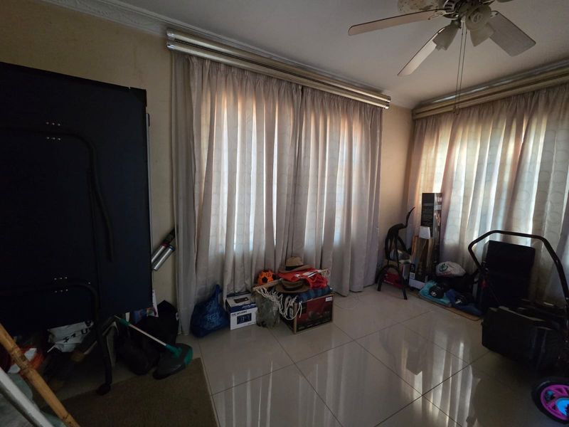 A living room area featuring tiled flooring and a ceiling fan, currently used for storage.
