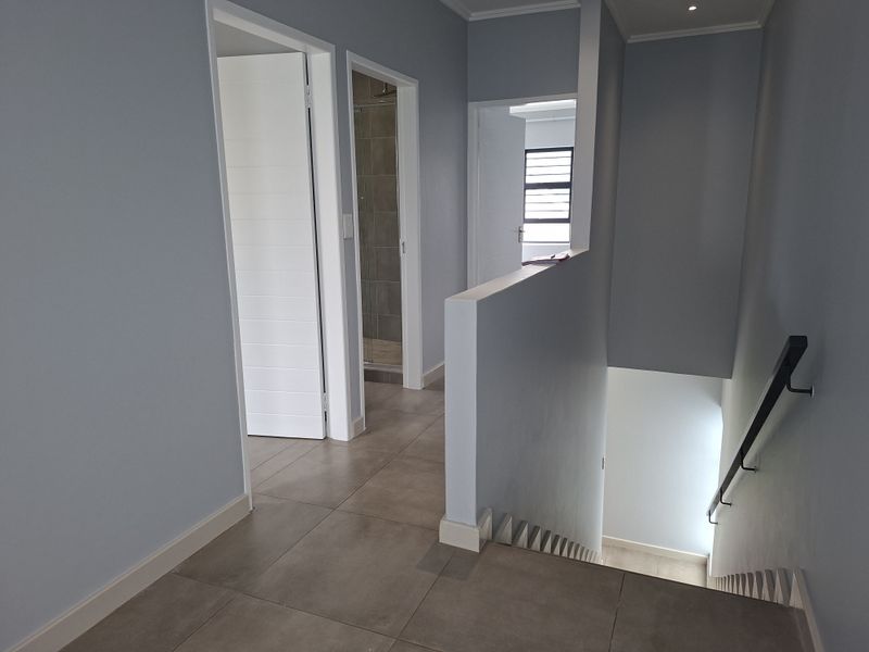 A clean, modern hallway featuring tiled flooring, a staircase with a handrail, and access to adjacent rooms.