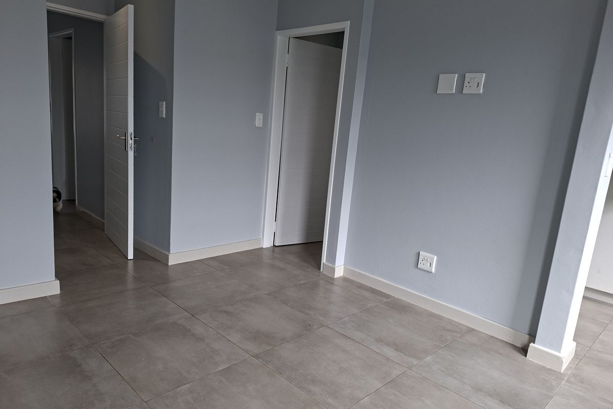 An empty, well-maintained living area featuring neutral grey walls, large format floor tiles, and multiple internal doorways.