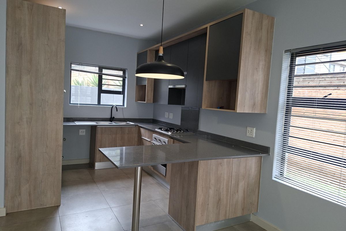Modern kitchen featuring wood-tone and dark grey cabinetry, stone countertops, integrated gas hob, oven, and sleek finishes in a bright, open-plan layout.