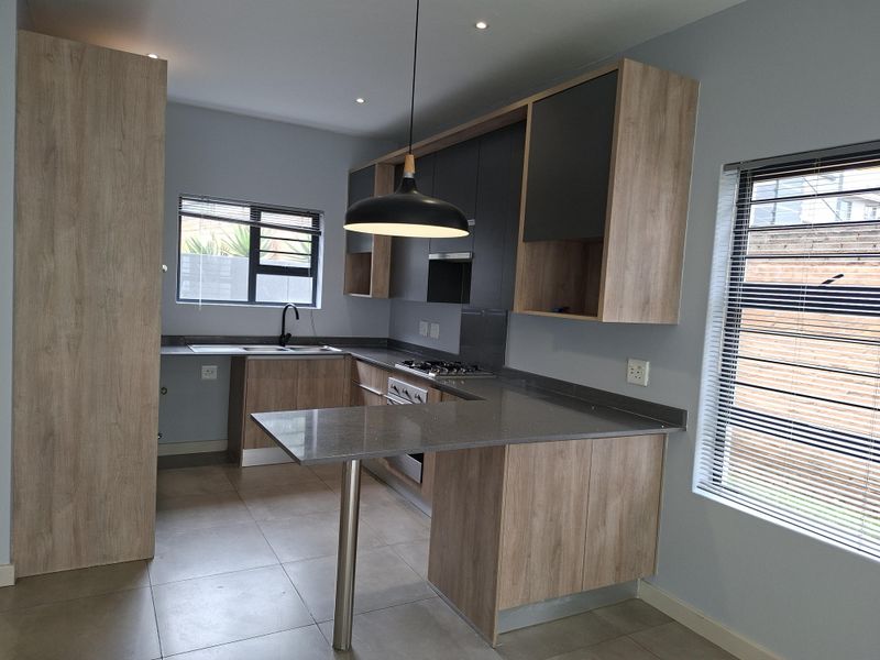 Modern kitchen featuring wood-tone and dark grey cabinetry, stone countertops, integrated gas hob, oven, and sleek finishes in a bright, open-plan layout.