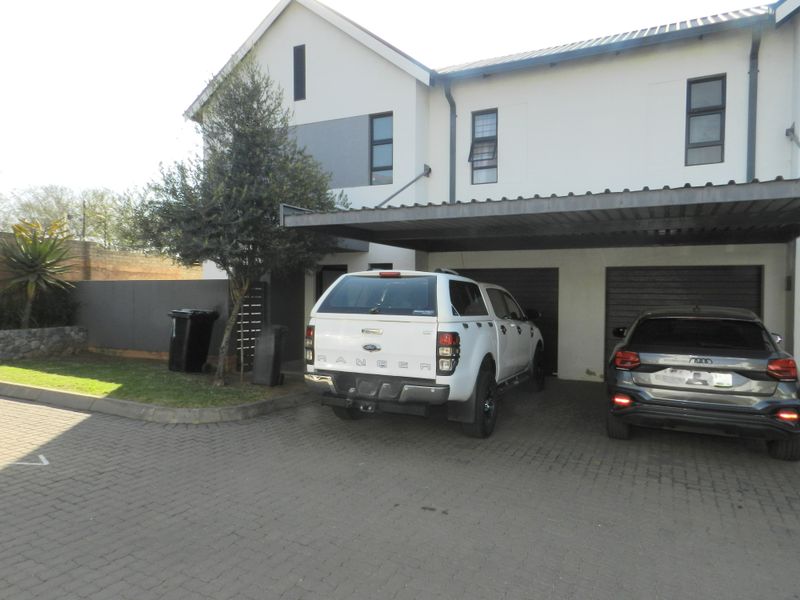 Front elevation of a townhouse featuring a double garage, covered carport, and paved driveway area.