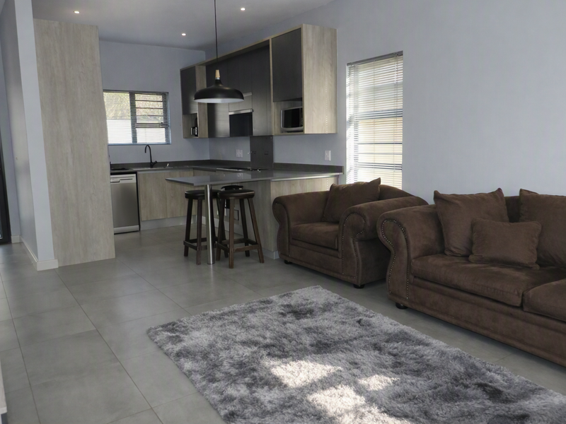Modern open-plan living area featuring a contemporary kitchen with built-in cabinetry, integrated island, and sleek tiled flooring throughout the combined space.