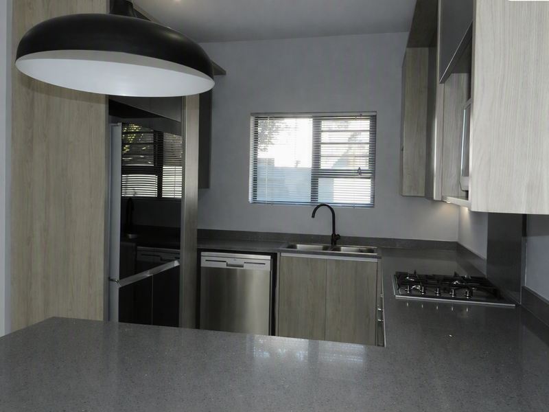 Modern kitchen featuring light wood-grain cabinetry, dark stone countertops, a gas hob, and integrated dishwasher, offering a clean and functional workspace.