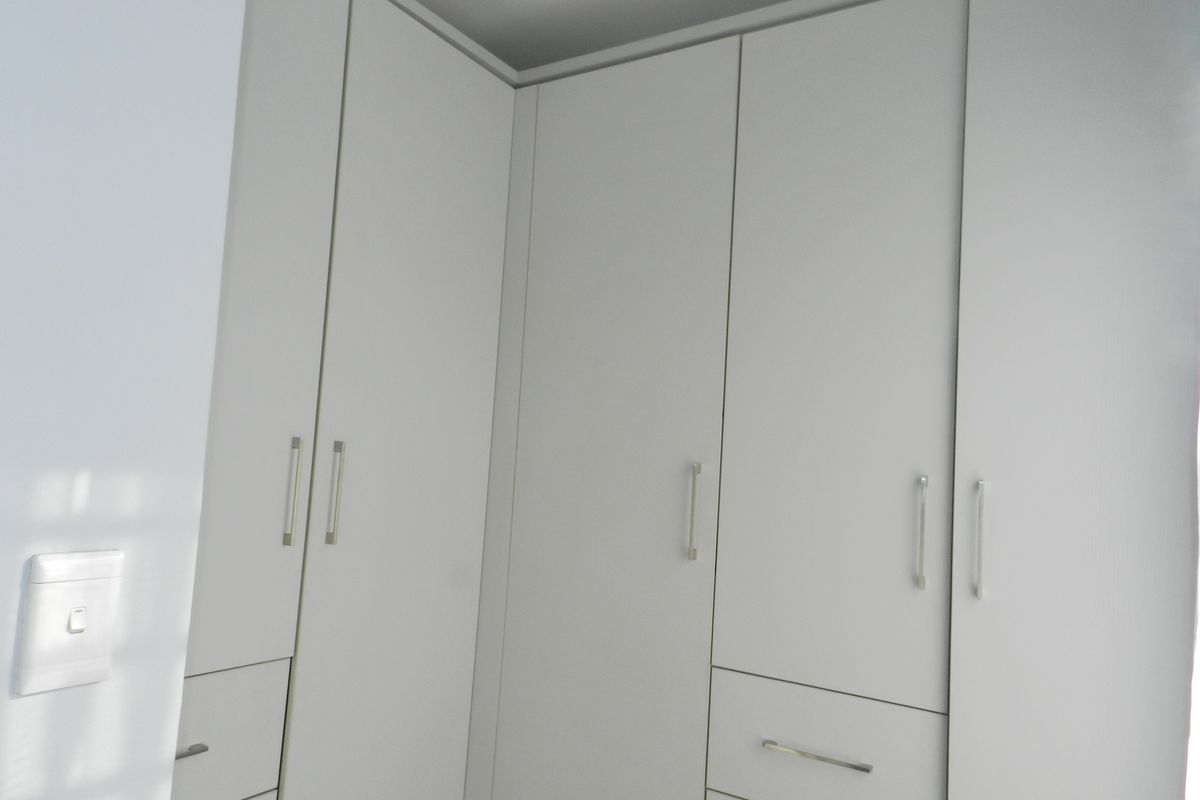 A bedroom featuring modern, white built-in cupboards with sleek metal handles, providing ample storage space.