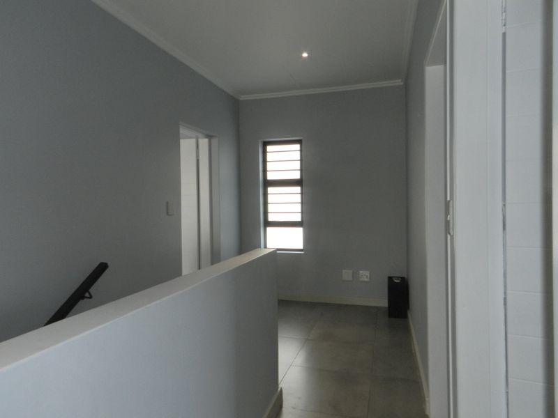 A clean and neutral upstairs landing or hallway featuring tiled flooring, a modern balustrade, and a louvre window providing natural light.
