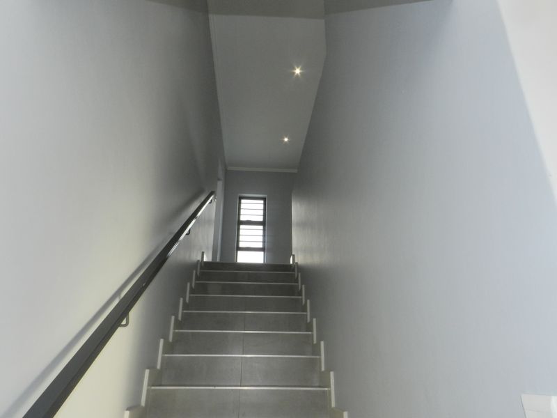 A modern, minimalist staircase featuring tiled steps, a sleek handrail, and recessed ceiling lighting, leading to an upper level with a window.