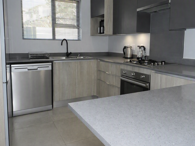 Modern kitchen featuring stone countertops, built-in oven, gas hob, extractor fan, and ample cabinetry with a clean, contemporary finish.