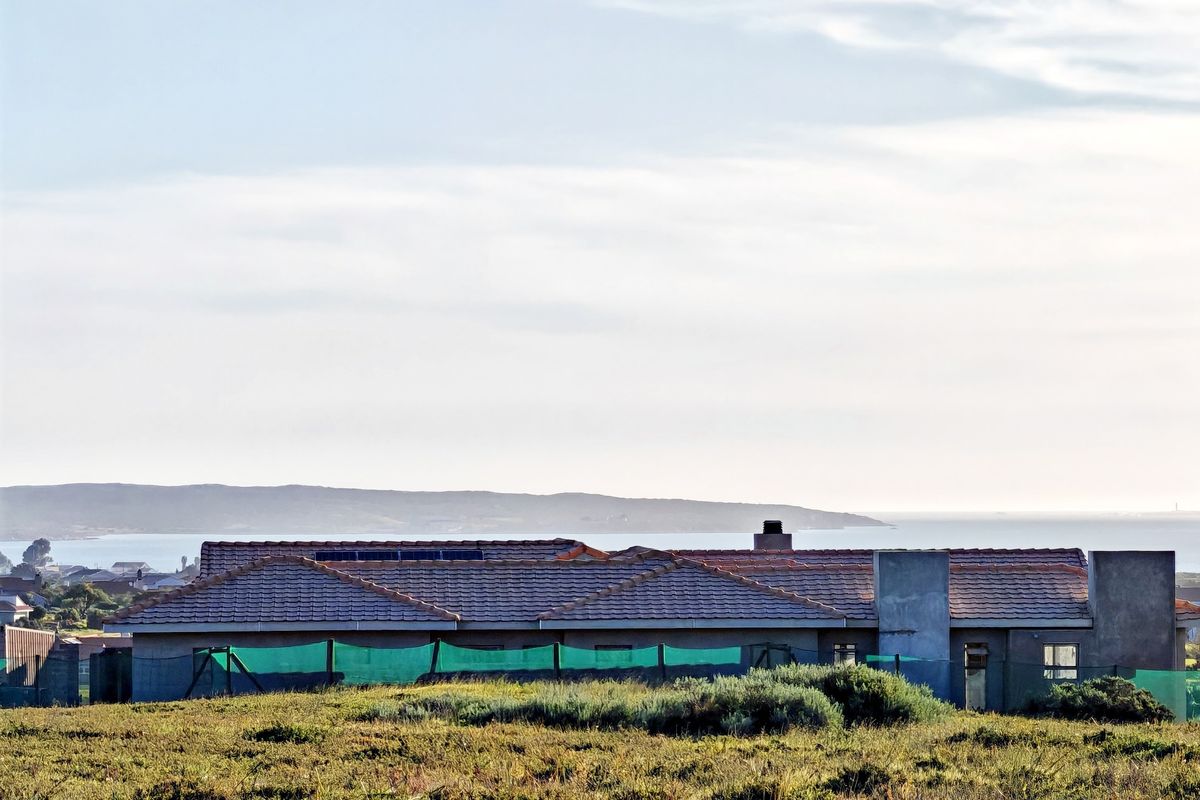 Rear view of a residential property featuring a tiled roof with solar panels, a chimney, and unfinished exterior wall surfaces overlooking a coastal landscape.