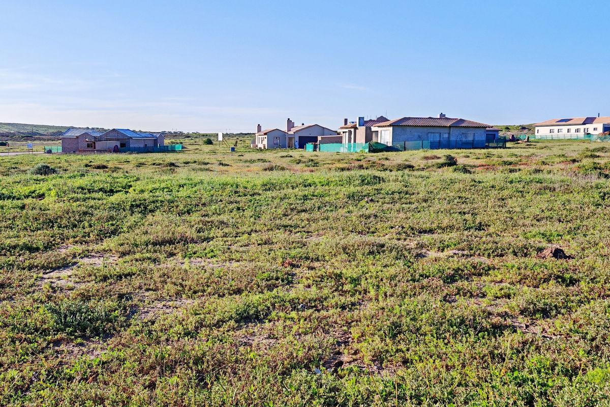 A wide-angle view of a vacant residential plot featuring natural vegetation with established neighboring homes visible in the background.