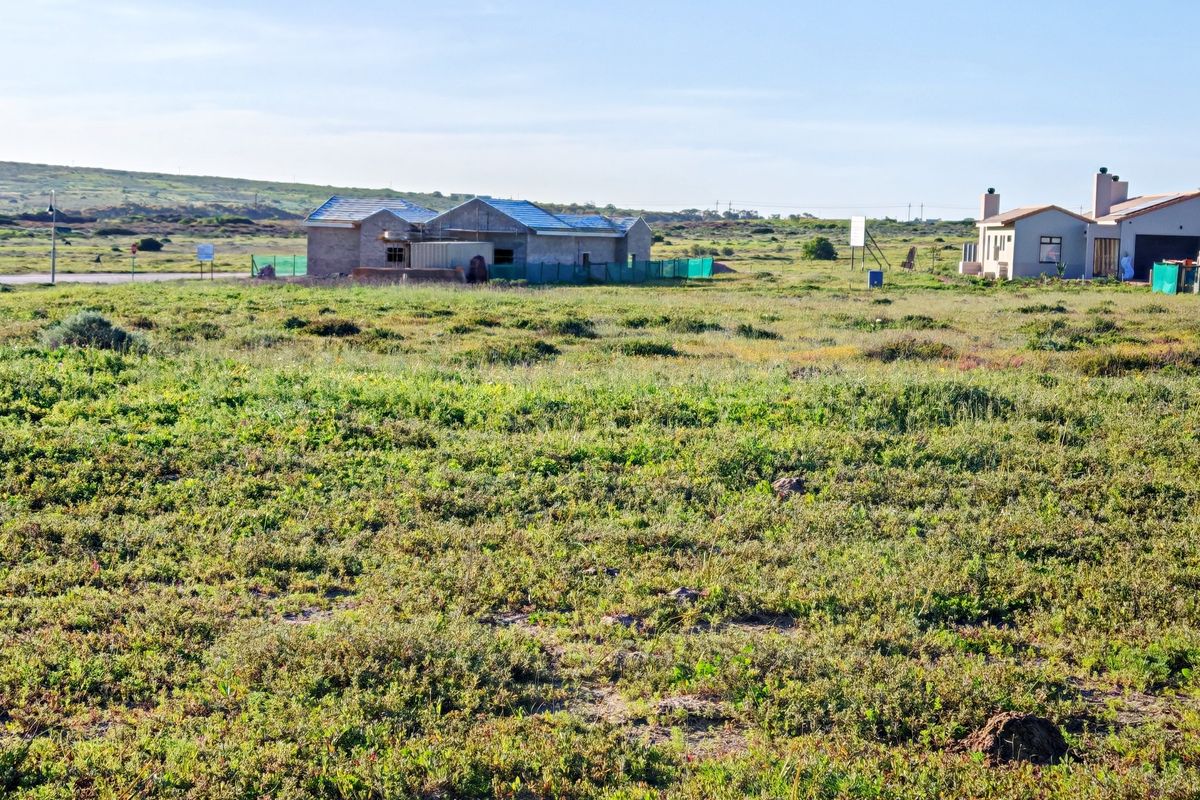A view of a vacant residential plot with natural vegetation, showing neighboring properties under construction in the background.