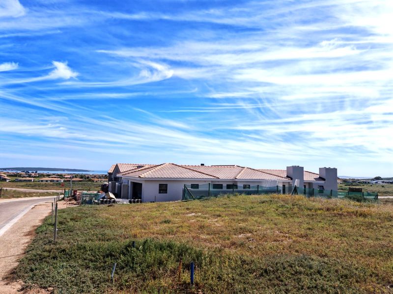A view of a residential property under construction, featuring a tiled roof, chimneys, and surrounding undeveloped land in a coastal setting.