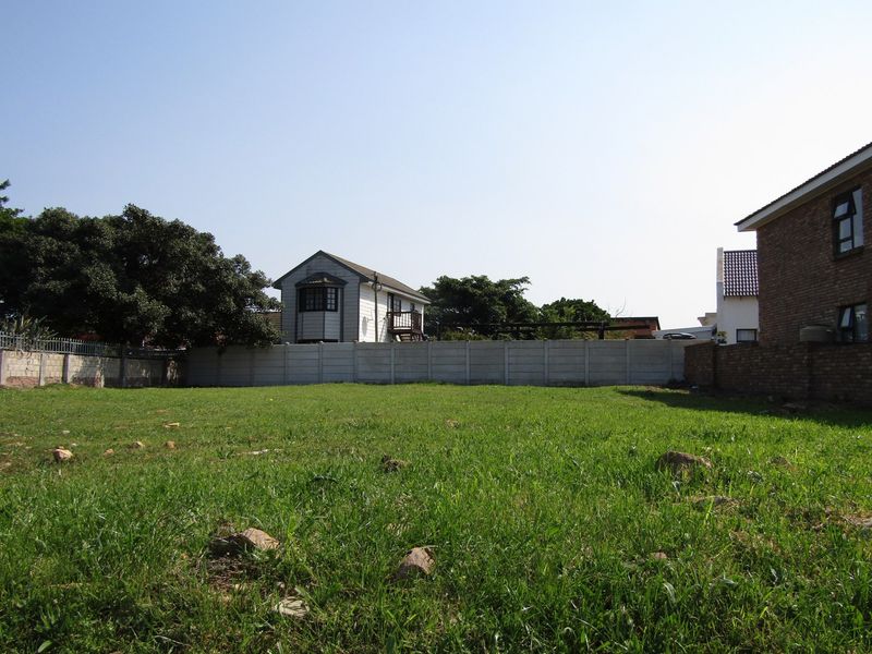 A vacant residential plot featuring a grassed area enclosed by precast concrete and brick boundary walls.