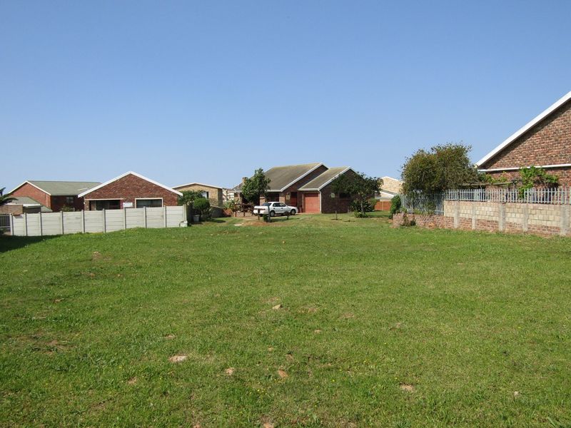 A view of a vacant residential plot featuring grass lawn and surrounding boundary walls with neighboring houses in the background.