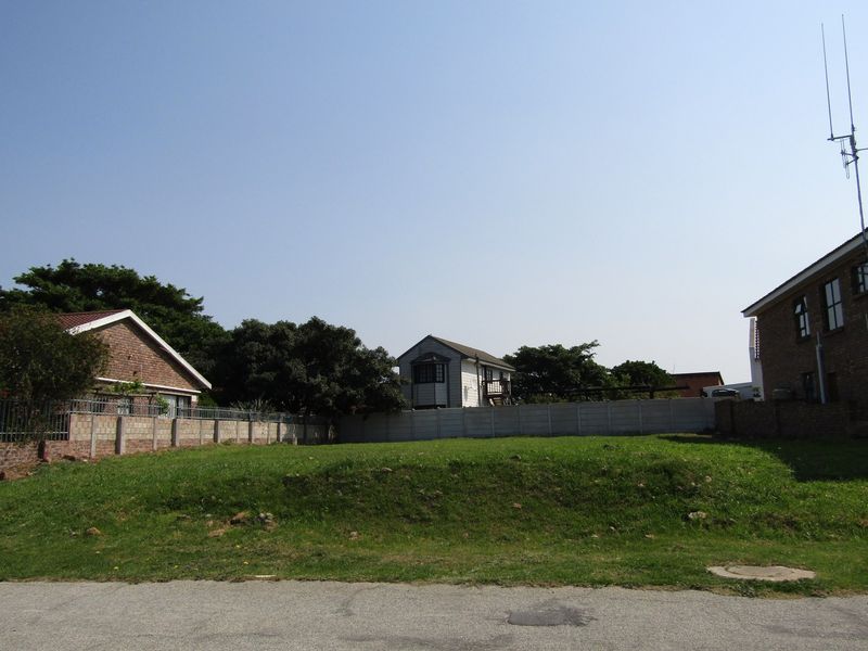 A vacant residential plot featuring a grass lawn, enclosed by precast concrete boundary walls, situated in a developed neighborhood.