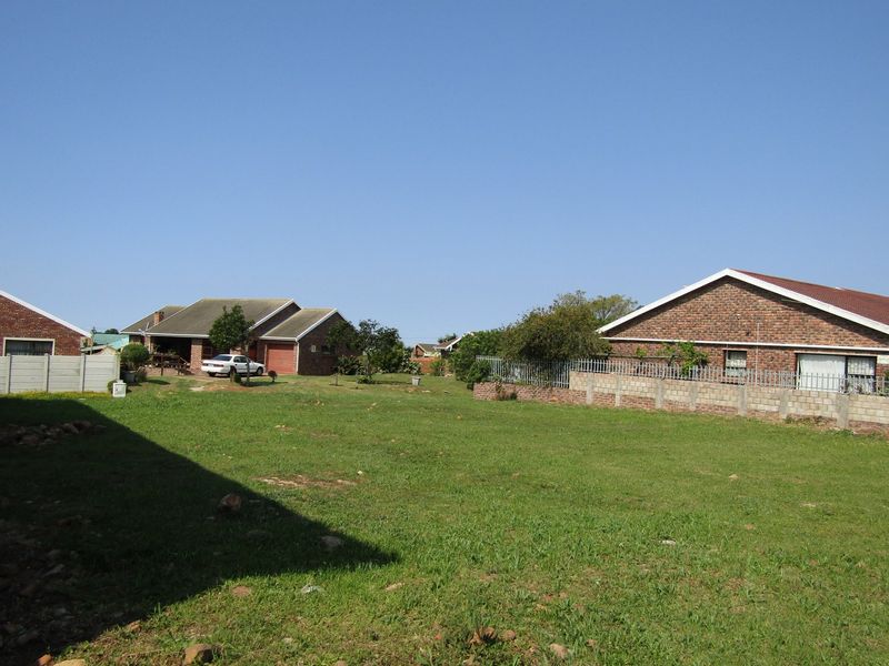 A view of a residential backyard area featuring a grass lawn, brick boundary walls, and metal fencing, with neighboring houses visible in the background.