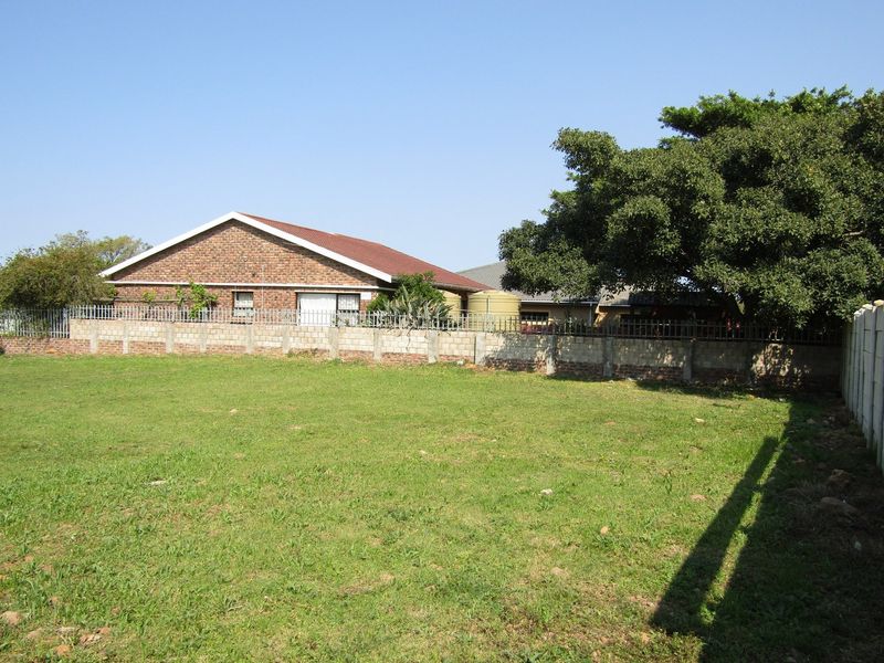 A view of the rear yard featuring a large grassed area, brick boundary wall with security fencing, and a water storage tank.