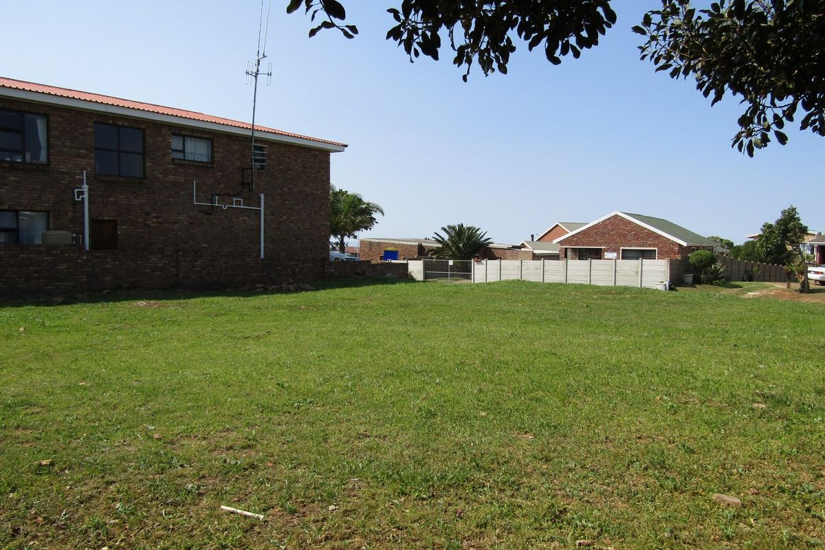 A vacant residential plot featuring a level grassed area, enclosed by a precast concrete boundary wall and adjacent to existing brick residential structures.