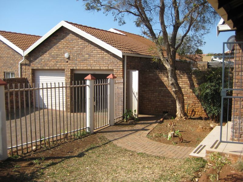 Front view of a brick-faced house featuring a double garage, paved driveway, and secure metal fencing with a garden walkway.