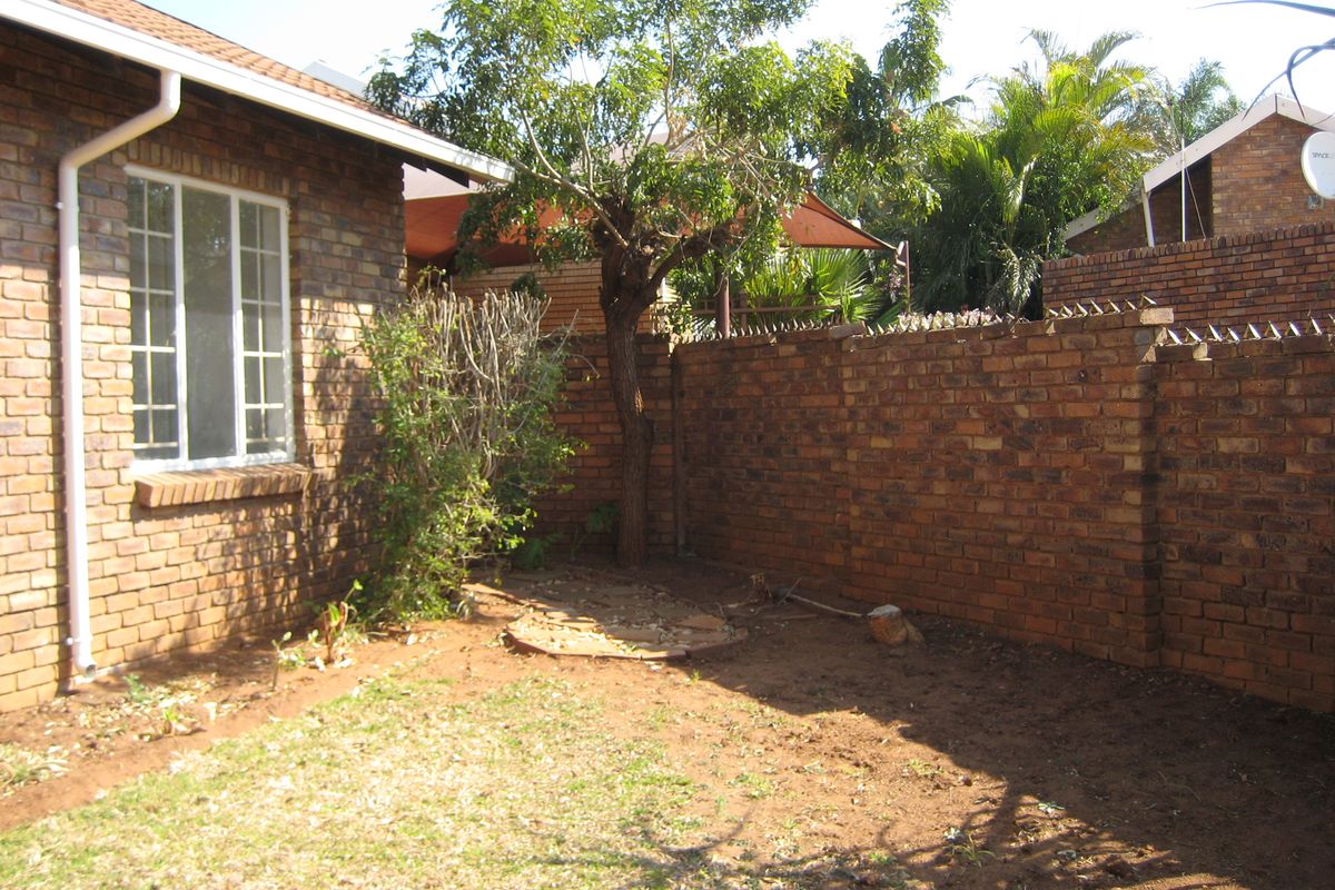 A rear garden area featuring face brick walls with security spikes and a small lawn space.