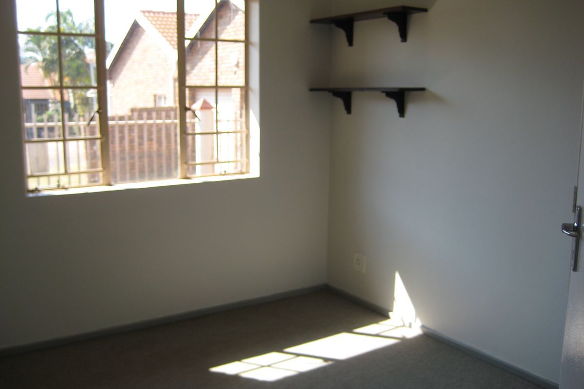 A vacant bedroom featuring carpeted flooring, a window with security bars, and built-in wall shelving.