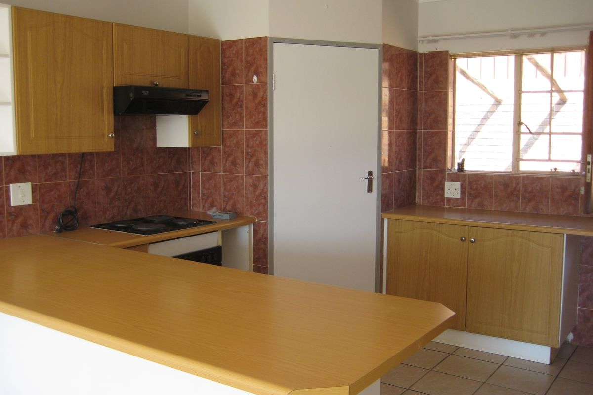 A functional kitchen featuring laminate cabinetry, tiled backsplash, and an electric hob, offering a clean, blank canvas for potential modern updates.